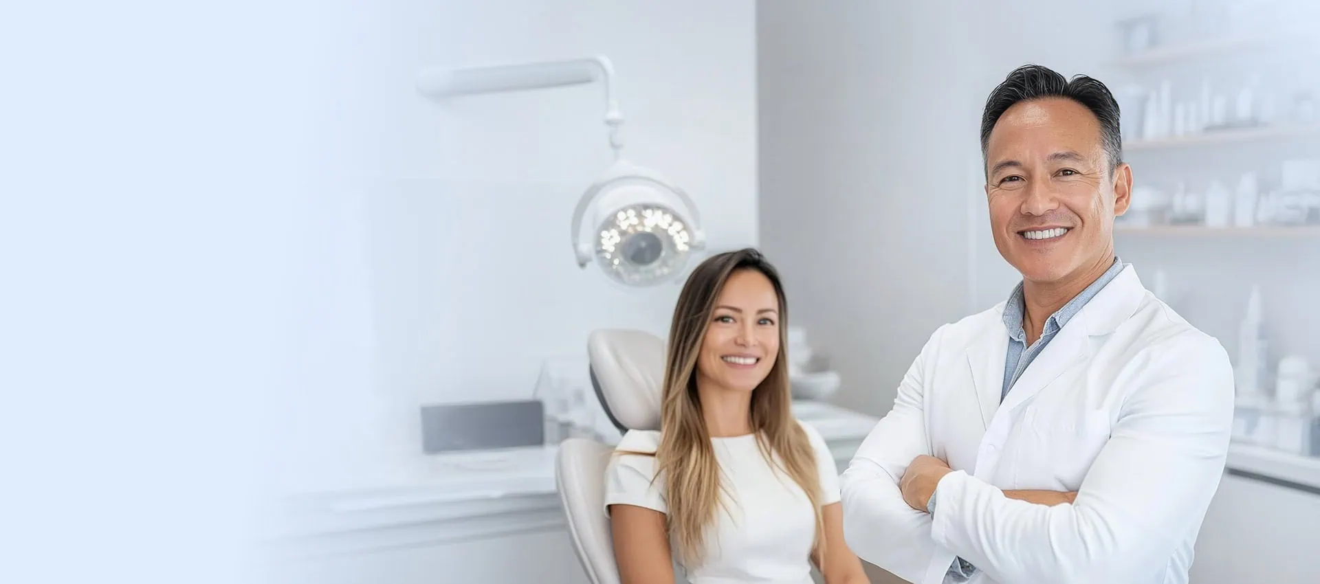 male dentist looking at camera smiling with female patient in background looking at camera smiling sitting in chair